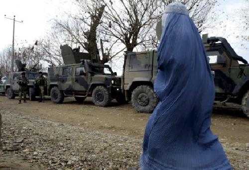 Una mujer afgana pasea frente a unos soldados